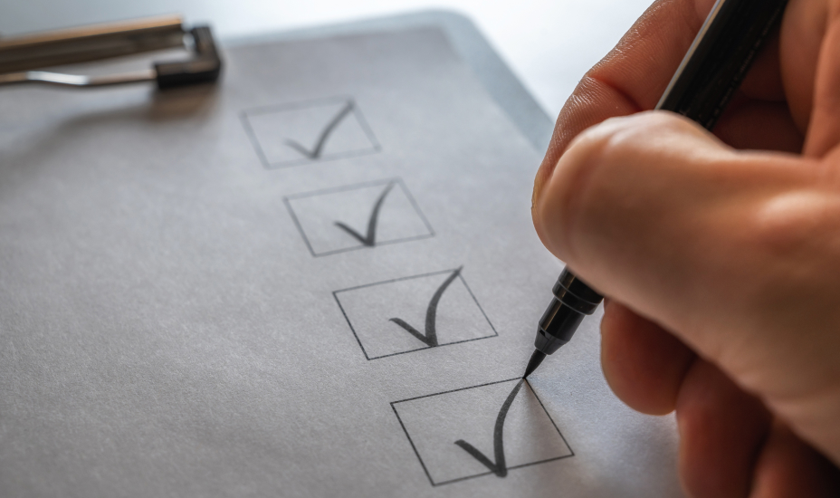 A hand holding a pen marks off checklist on a clipboard