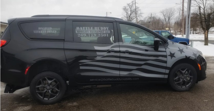Battle Buddy Mobility Transport Van. Black van with white American flag emblem and the Battle Buddy contact information. The back window says "Disabled Veteran Owned"
