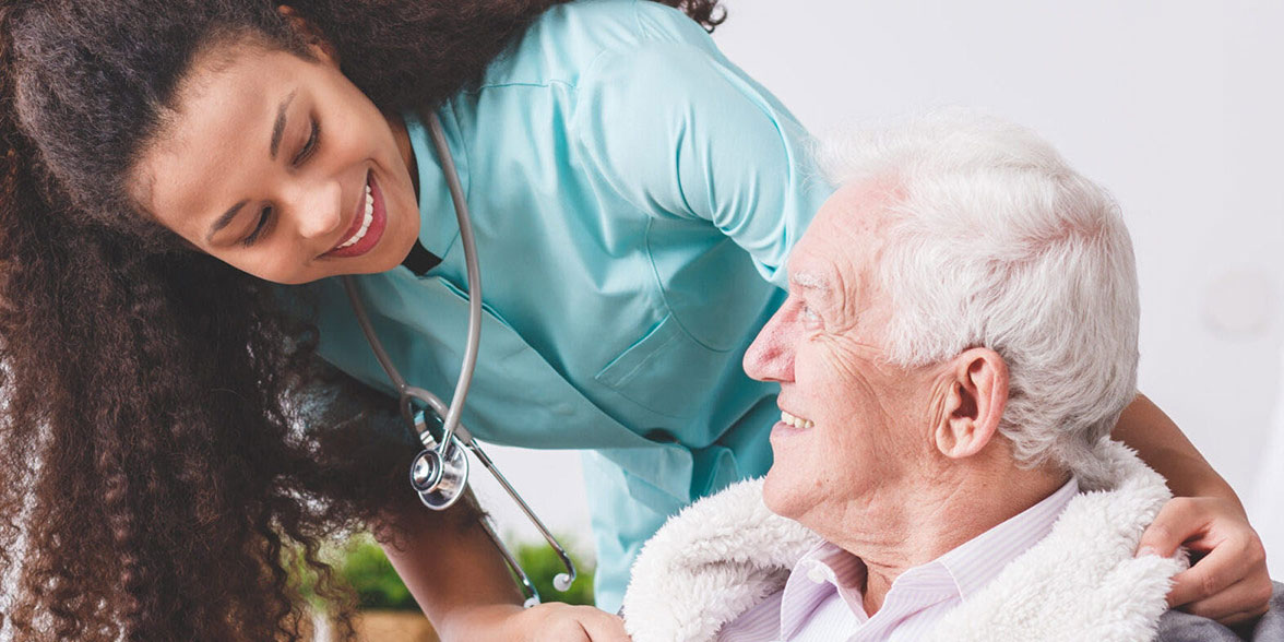 Panorama of a happy nurse with a stethoscope covering an elderly man with a blanket