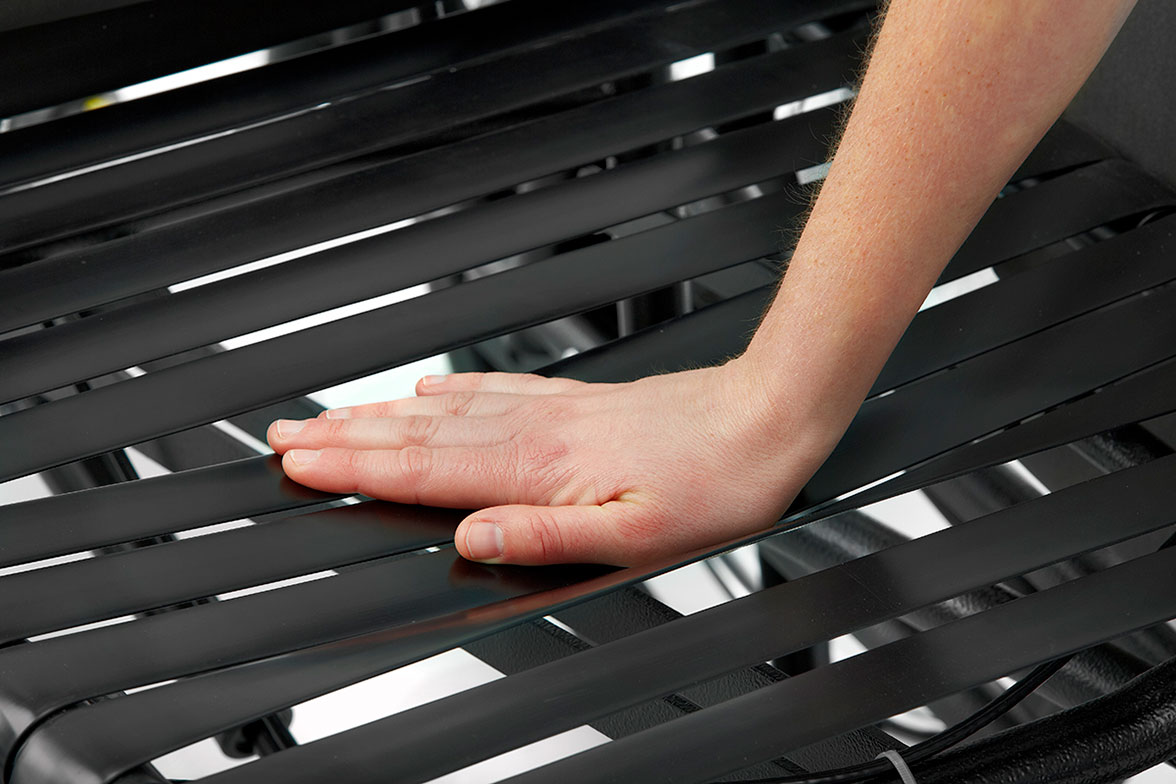 A hand gently compresses the Comfort Tension Seating System straps of a Broda wheelchair to demonstrate their pressure relieving qualities.