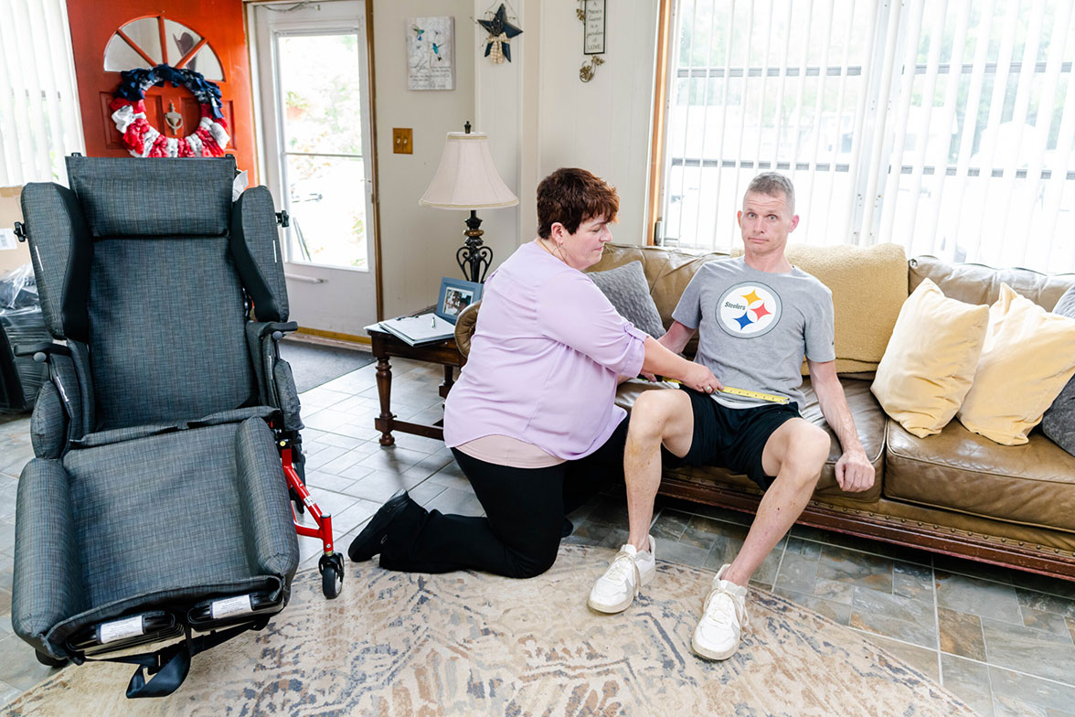 Occupational therapist measures a young man to determine the right size Broda wheelchair.