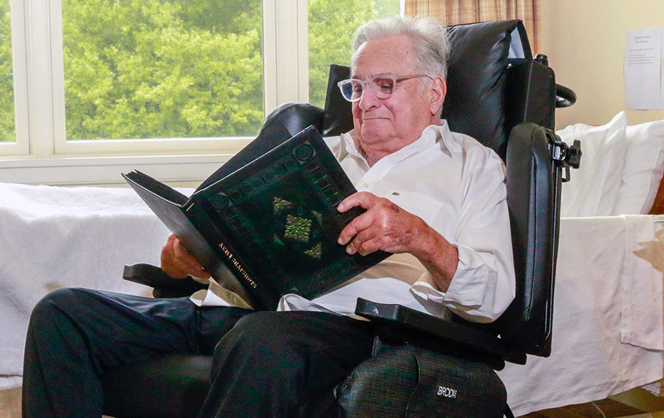 Elderly man sitting in a Synthesis Positioning Wheelchair while holding a book