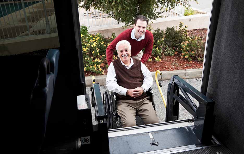 Young man helping an older gentleman in wheelchair into a transport vehicle