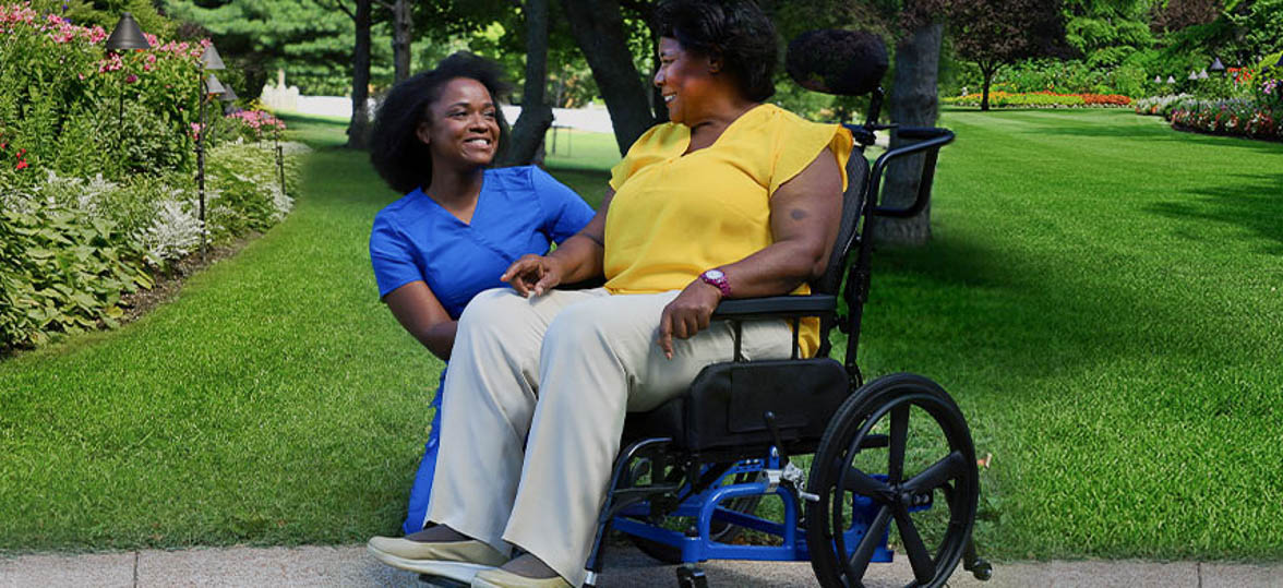 A caregiver and a patient in a wheelchair enjoy time together outside