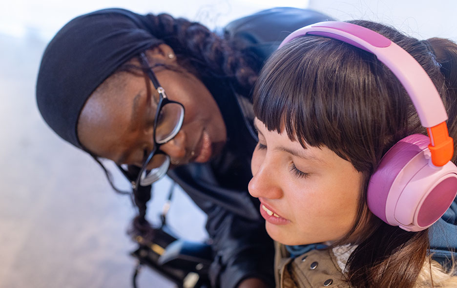 A young girl with autism wearing headphones with her caregiver close by