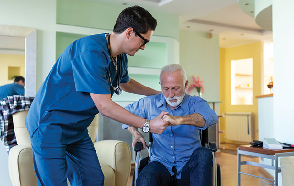 A healthcare worker helping a senior man in an out of a wheelchair while waiting in the lobby of a care facility