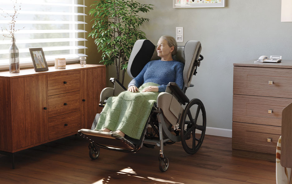 A 3D rendering of a senior woman resting in a Broda wheelchair inside her care facility bedroom