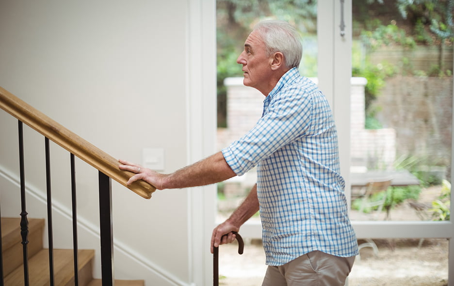 Older man holding a cane while looking hesitantly at a staircase